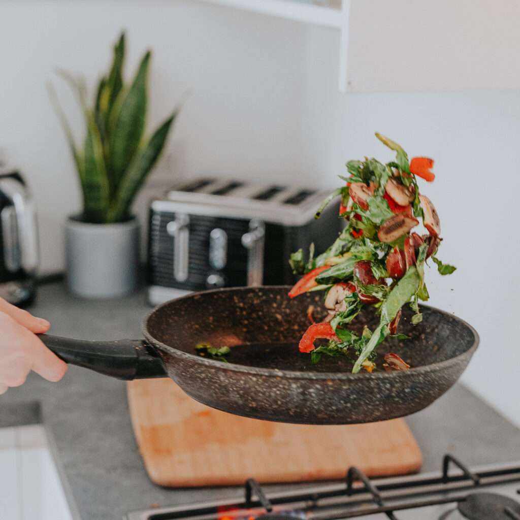 Vegetables are being tossed in a frying pan in a kitchen in an act of mindfulness.