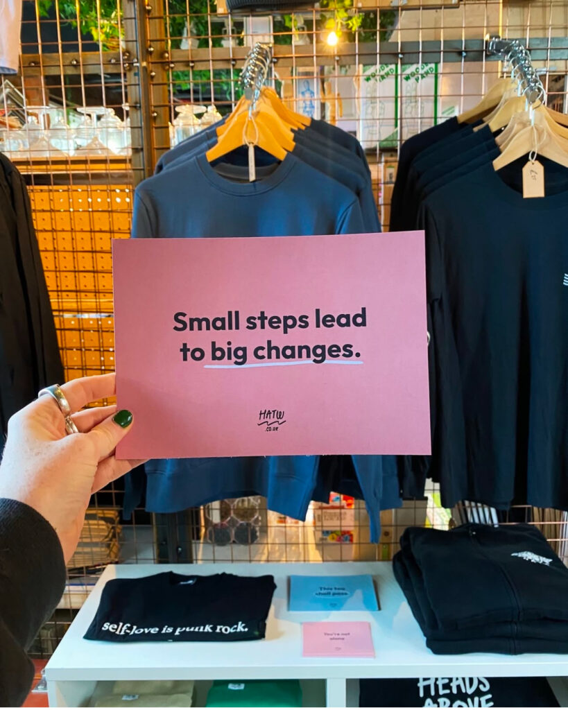 A hand holds a pink postcard that reads "small steps lead to big changes"